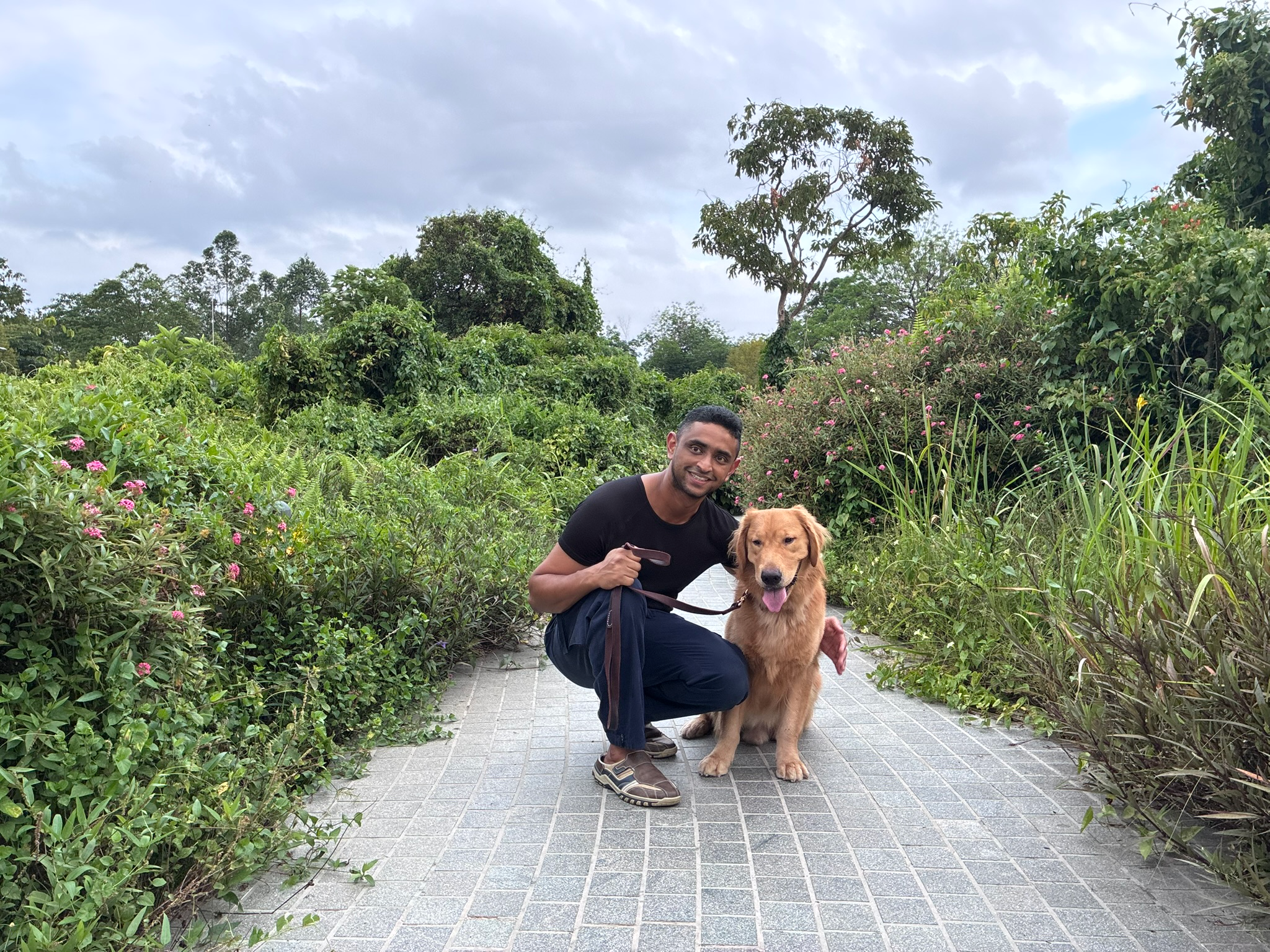 Shawn crouched beside a Golden Retriever on a garden path in Singapore — arm around the dog, both relaxed and looking at the camera